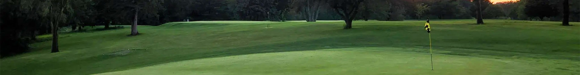 A stunning panoramic view of a golf course at sunset, featuring a lush putting green and scenic hills.